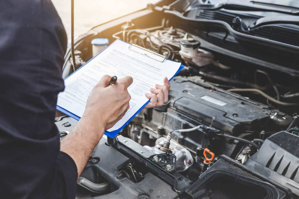 Automobile mechanic repairman checking a car engine with inspecting writing to the clipboard the checklist for repair machine, car service and maintenance.